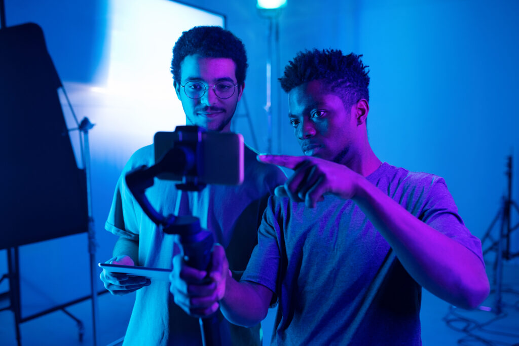 Zwei junge Männer in einem Studio prüfen gemeinsam den Bildschirminhalt eines Smartphones, das auf einem Gimbal befestigt ist.